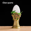 A clear quartz crystal is displayed atop a golden tree of life chime made of natural materials.