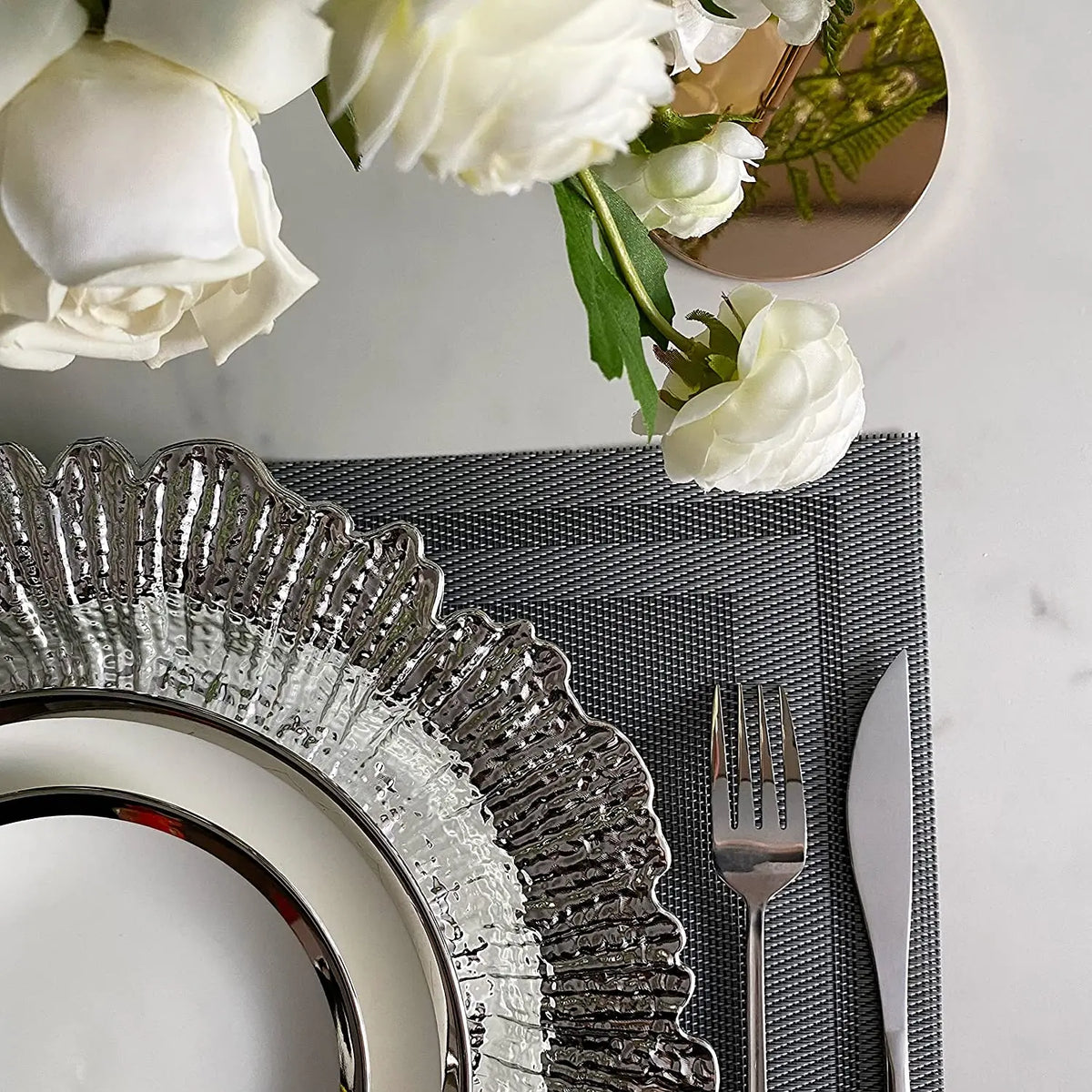 Elegant gold charger plates with silver detailing and white roses on a marble surface.