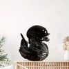 Black resin statue of an alien duck with textured scales sitting on a wooden surface.