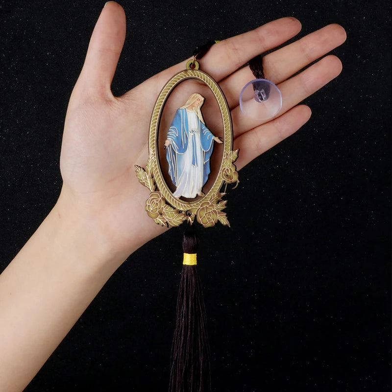 A hand holds a wooden pendant ornament of Our Lady of Grace with a glass bead and gold-colored wire.