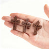 Trois petits pendentifs en bois de forme de croix sont tenus dans la main d'une personne sur un fond blanc.
