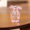 A clear pink glass vase shaped like a bottle sits on a wooden surface.