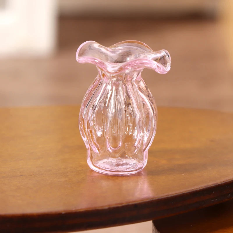 A clear pink glass vase shaped like a bottle sits on a wooden surface.