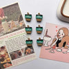 A set of green and brown coffee bean fridge magnets with a leaf shape displayed on a pink card.