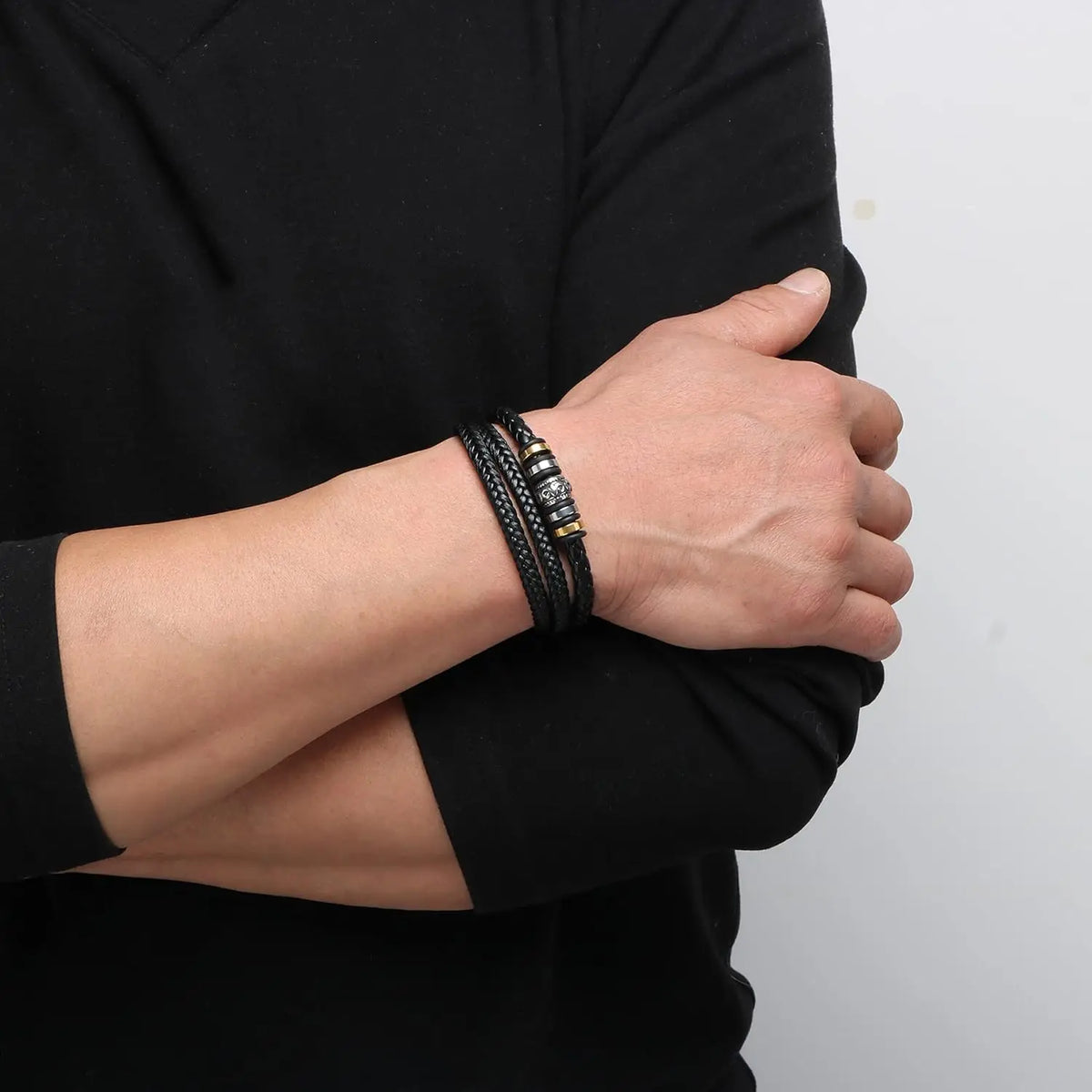 A close-up of a hand wearing a black braided leather cuff bracelet on a wrist, against a dark background.