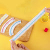 A hand holds a white and blue reusable elastic food cover, demonstrating its flexible fresh-keeping lid for containers.