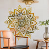 Un grand autocollant murale lotus mandala or et noir est exposé au-dessus d'une chaise et d'une table en bois.
