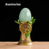 A smooth, light green Aventurine crystal is displayed atop a brass tree of life chime.