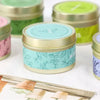 A collection of natural soy wax travel candles in various colors and designs, including pink, mint green, and lavender.