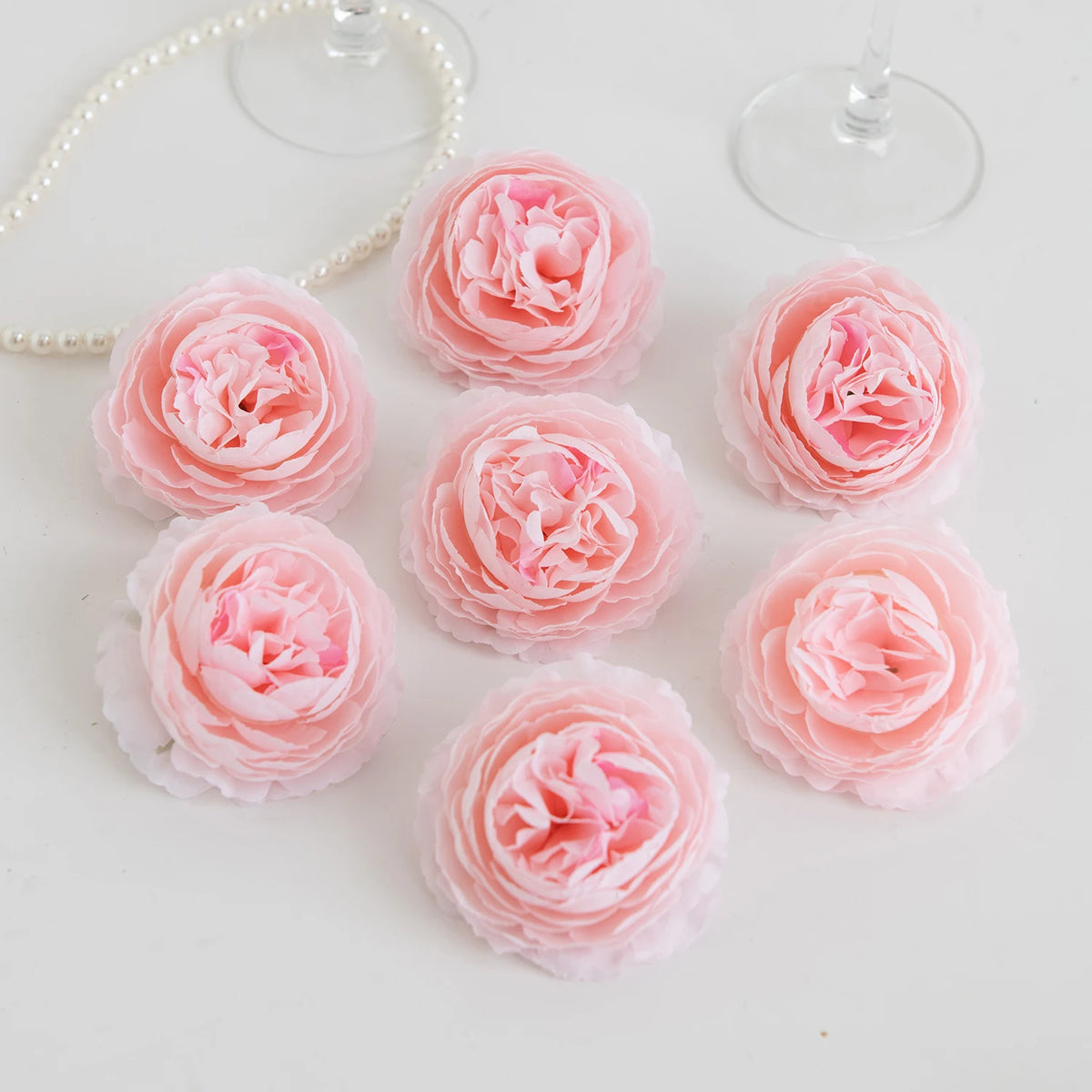 A collection of soft pink silk peony artificial flowers arranged on a white surface.