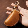 A brown leather key pouch with a brass carabiner is held in a hand.