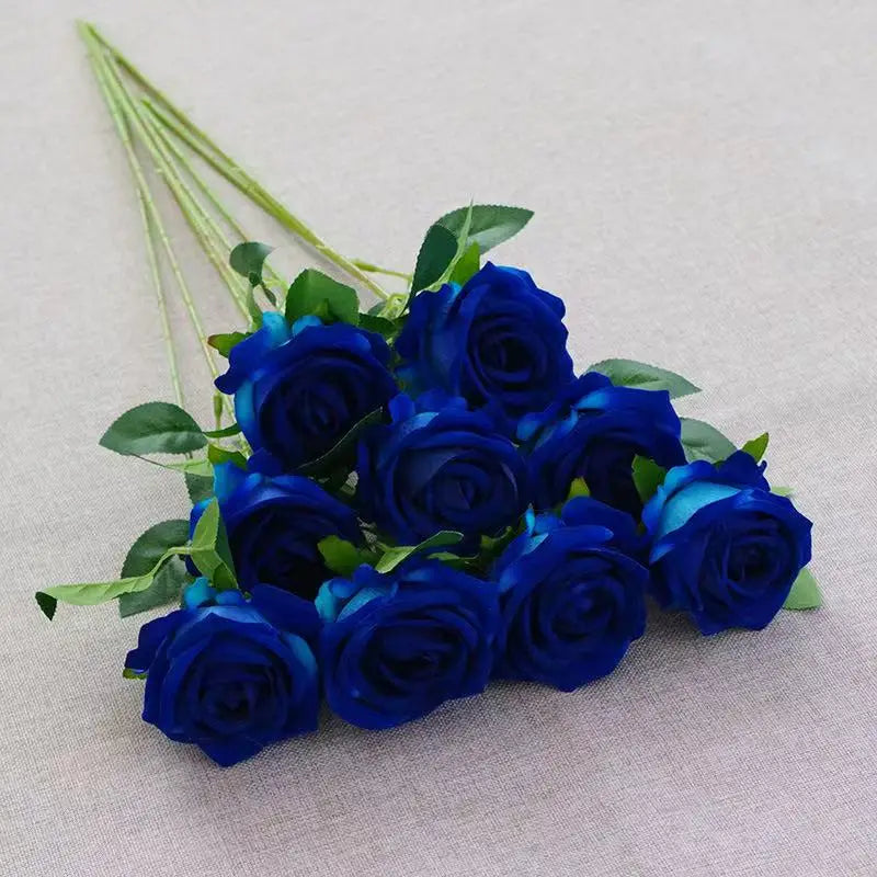A bouquet of deep blue velvet artificial roses with green stems arranged on a light fabric.