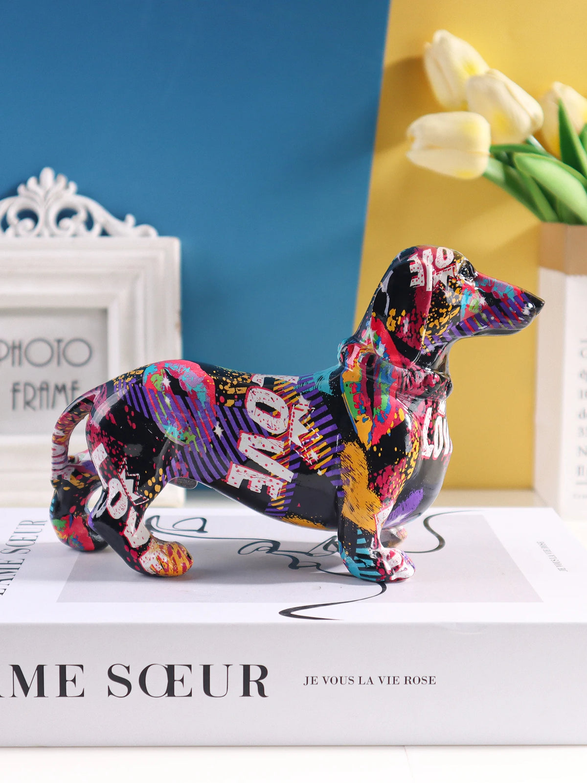 A colorful dachshund resin figurine in various bright colors standing on a white box.