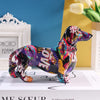 A colorful dachshund resin figurine in various bright colors standing on a white box.