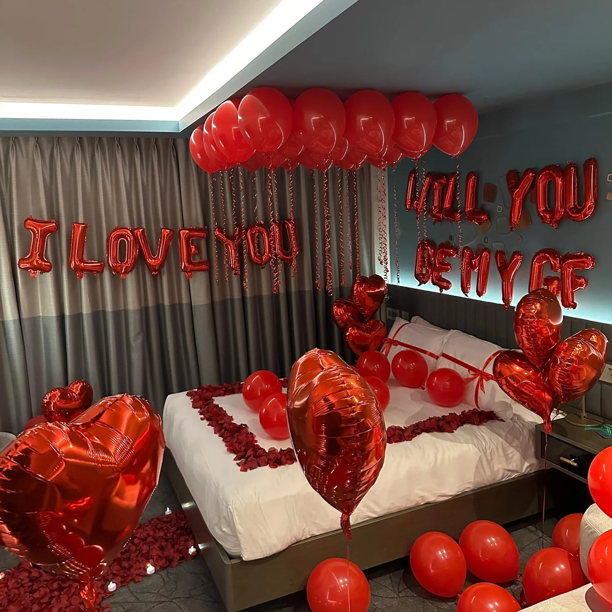 A display of red heart-shaped foil balloons spelling out I LOVE YOU and I LOVE MY GF decorating a bedroom.