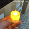 A hand holds a glowing yellow LED flickering candle against a blurred background.