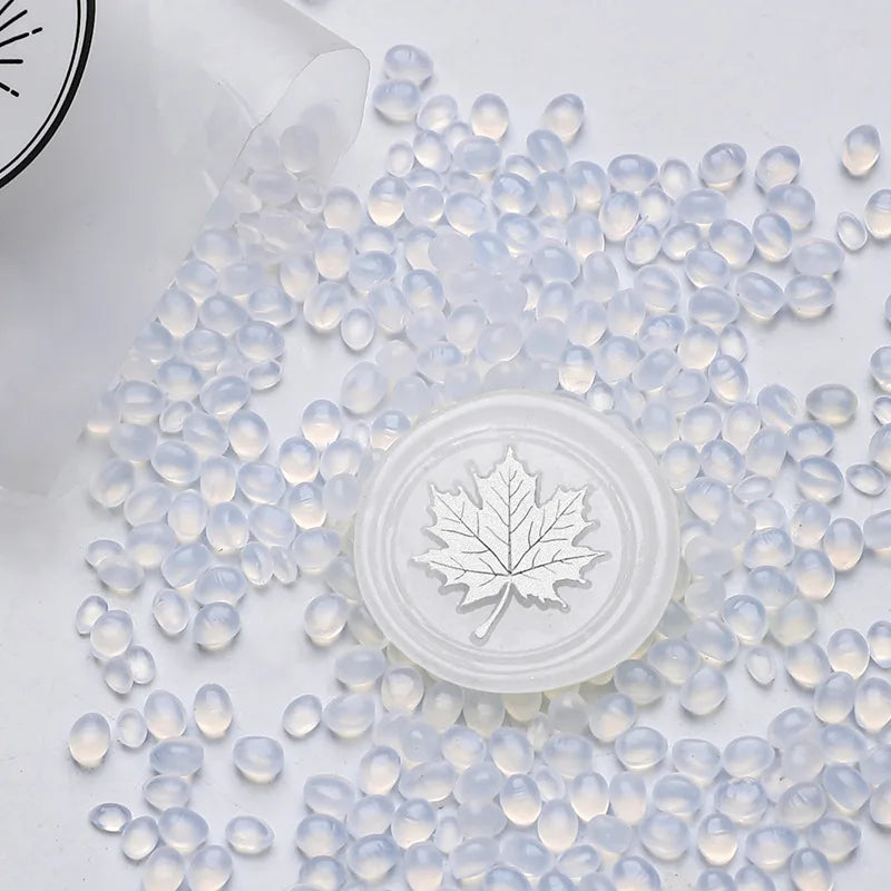 Clear wax sealing beads scattered on a white surface with a round silicone stamp in the center.