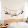 A bedroom wall decorated with a beaded photo display garland featuring small wooden clips and framed photos above a wooden be