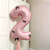 A large pink foil balloon shaped like the number 2 with black bows, hanging on a white door frame.