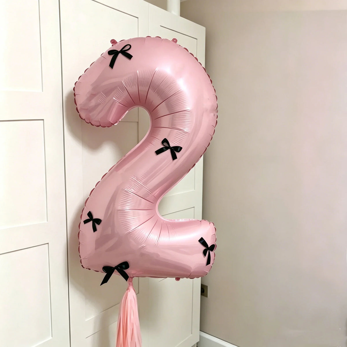 A large pink foil balloon shaped like the number 2 with black bows, hanging on a white door frame.