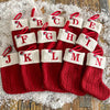 A collection of red knitted socks shaped like letters A through N, used as Christmas alphabet ornaments.
