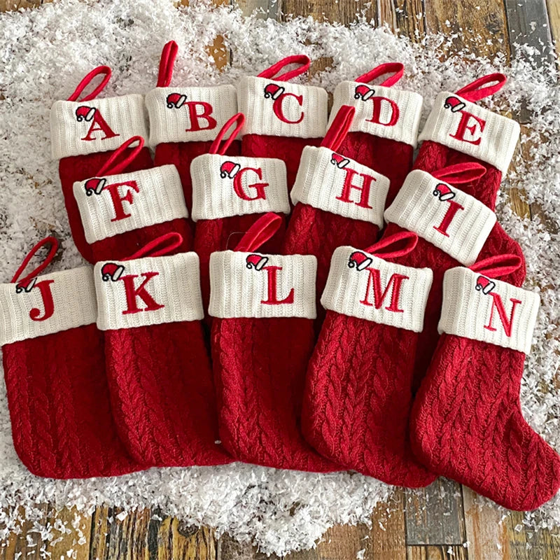 A collection of red knitted socks shaped like letters A through N, used as Christmas alphabet ornaments.