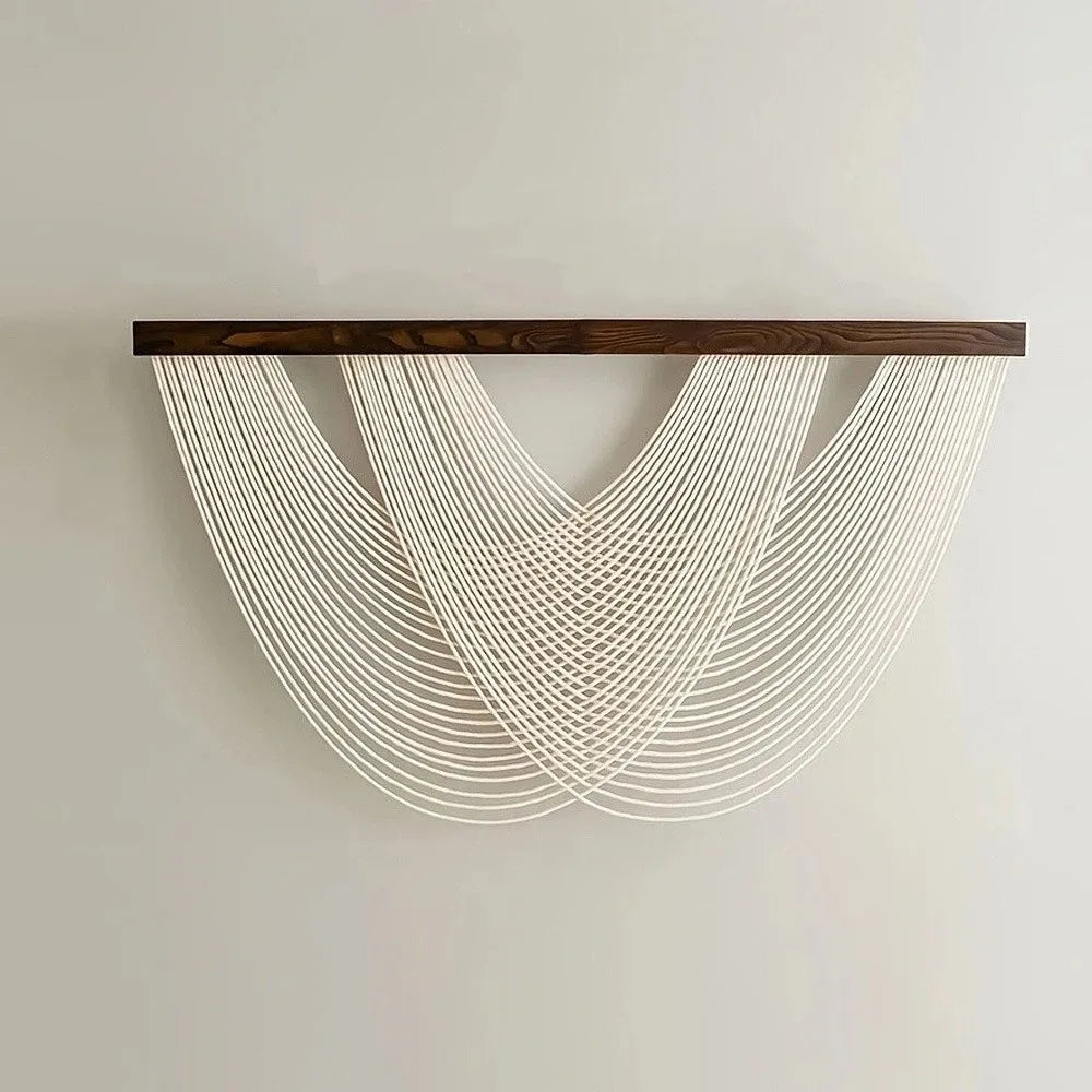 Bohemian macrame wall tapestry featuring white knotted cords suspended from a dark wooden bar.