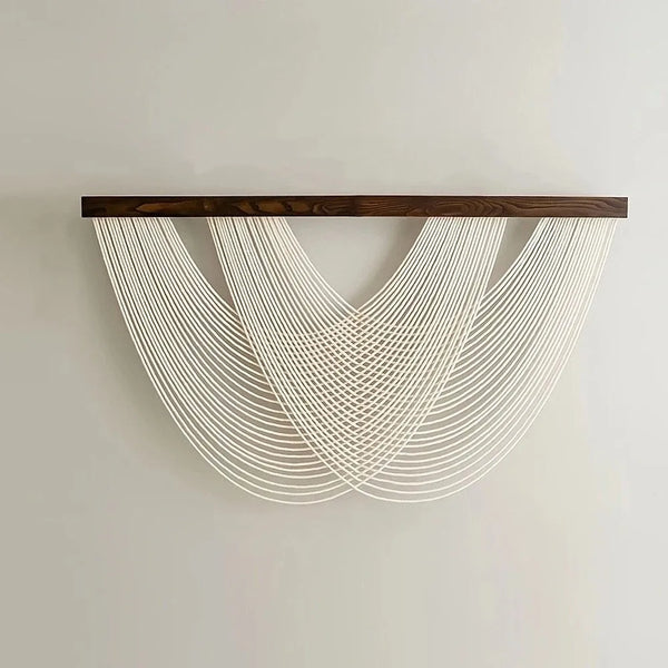 Tapis mural macramé bohème avec des cordes nouées blanches suspendues d'une barre en bois foncé.