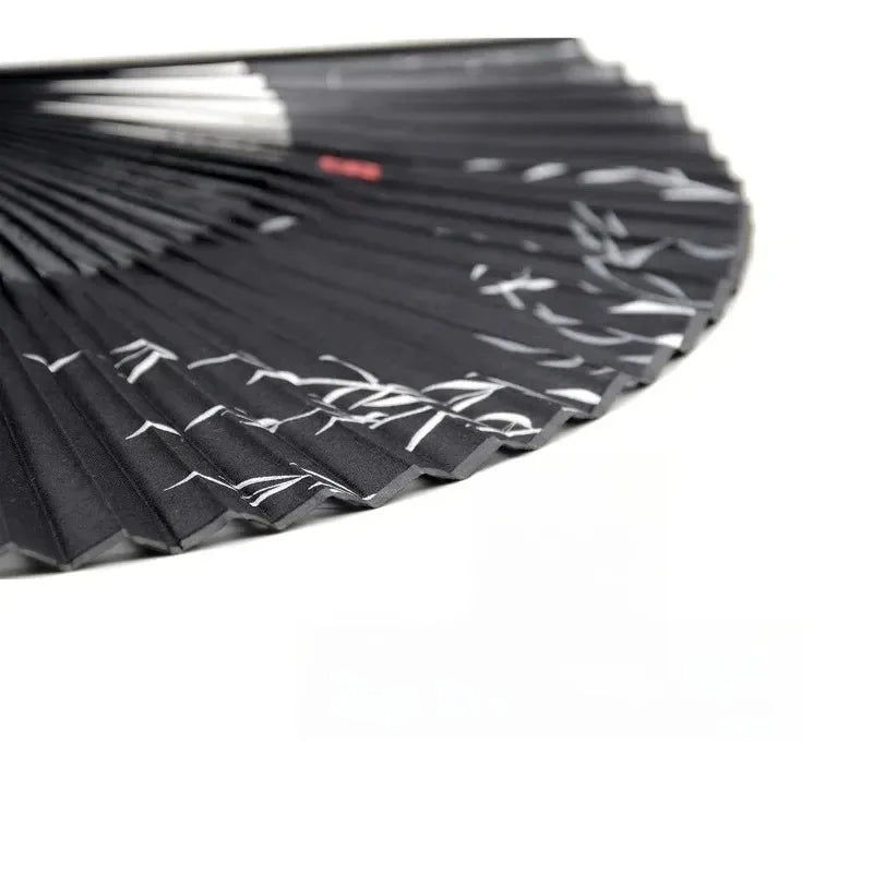 A close-up of a black vintage bamboo folding hand fan with delicate white patterns.