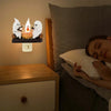 A night light featuring white ghost figures with a flickering orange flame on a wooden shelf.