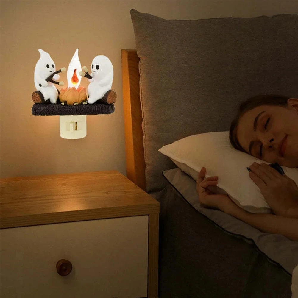 A night light featuring white ghost figures with a flickering orange flame on a wooden shelf.