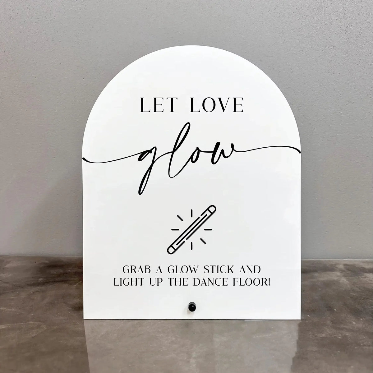 White acrylic sign with black script text that reads Let Love Glow and features an illustration of a glow stick.