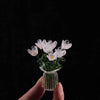 Handcrafted mini glass flower sculpture with white and yellow petals in a clear glass vase against a black background.
