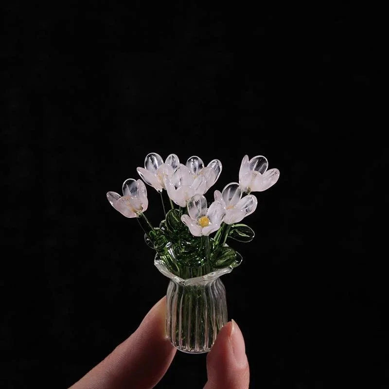 Handcrafted mini glass flower sculpture with white and yellow petals in a clear glass vase against a black background.