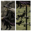 A portrait of an old witch in a hat and dark robes, next to a garden decor featuring bat silhouettes on a metal stand.