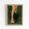 A framed canvas art print featuring a black cat standing on green grass.