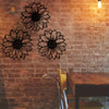 A set of black metal sunflower wall decor cutouts mounted on a rustic brick wall.
