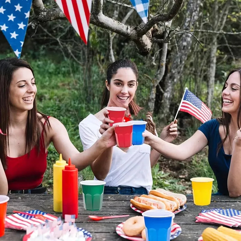 Four women laughing outdoors holding red and blue plastic shot cups for a party event.