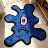 A blue cartoon monster rug with pink eyes and purple mouth on a light floor.