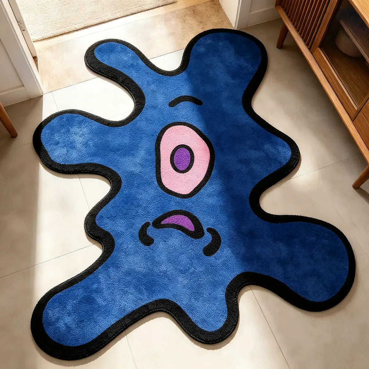 A blue cartoon monster rug with pink eyes and purple mouth on a light floor.