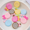 A collection of 20 colorful swirl-shaped resin candy charms in pink, yellow, and blue on a white plate.