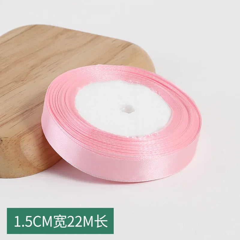 Roll of pink silk satin ribbon with a wooden block in the background