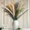 A bouquet of natural dried flowers featuring beige grasses, purple lavender, and silvery-green eucalyptus in a white vase.