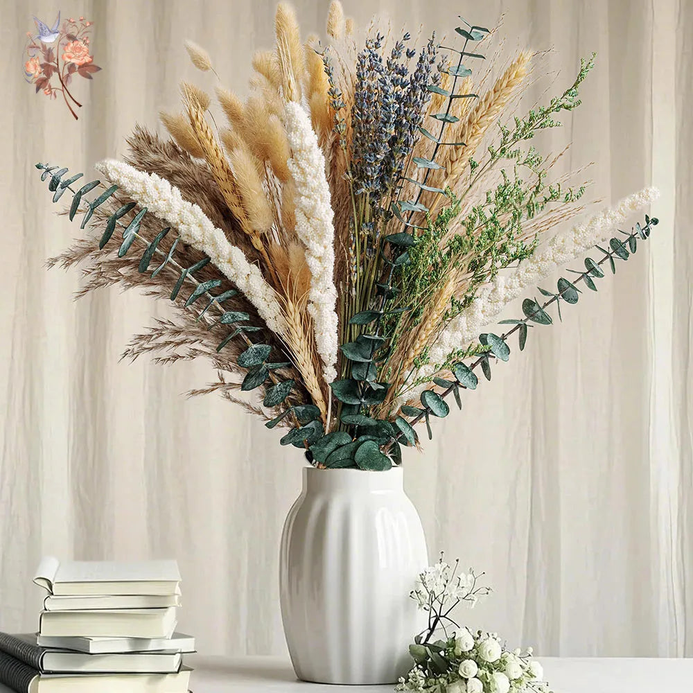 A bouquet of natural dried flowers featuring beige grasses, purple lavender, and silvery-green eucalyptus in a white vase.