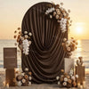 A dark draped arch cover decorated with white and beige floral arrangements for a wedding or event backdrop.