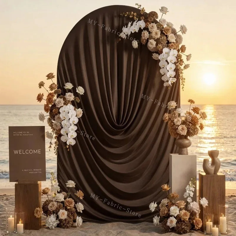 A dark draped arch cover decorated with white and beige floral arrangements for a wedding or event backdrop.