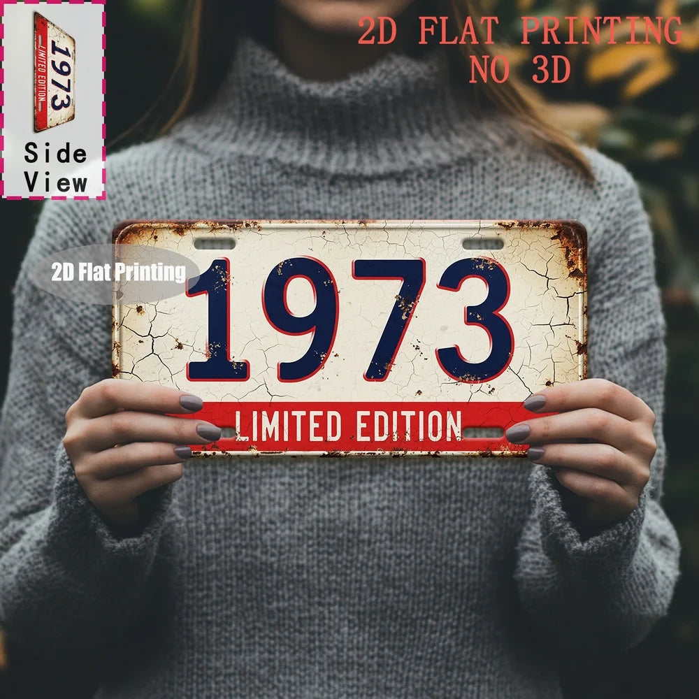 A person holds a vintage metal tin sign with the year 1973 printed on it, against a gray sweater.