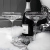 A black and white high heels art print is displayed next to a bottle of Piper-Heroick and two glasses on a table.