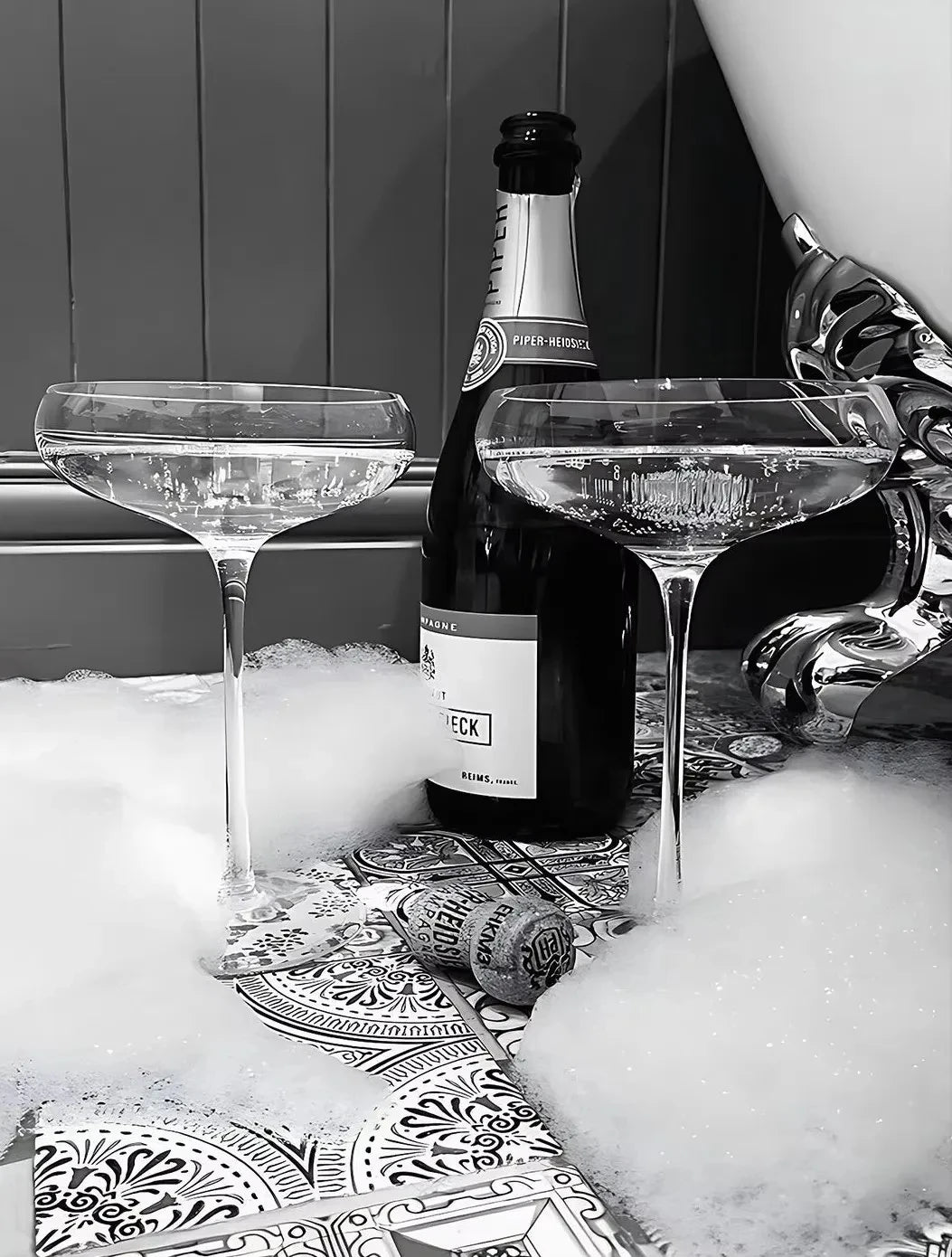 A black and white high heels art print is displayed next to a bottle of Piper-Heroick and two glasses on a table.
