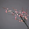 A delicate branch of artificial plum blossoms with pink and white flowers against a gray background.